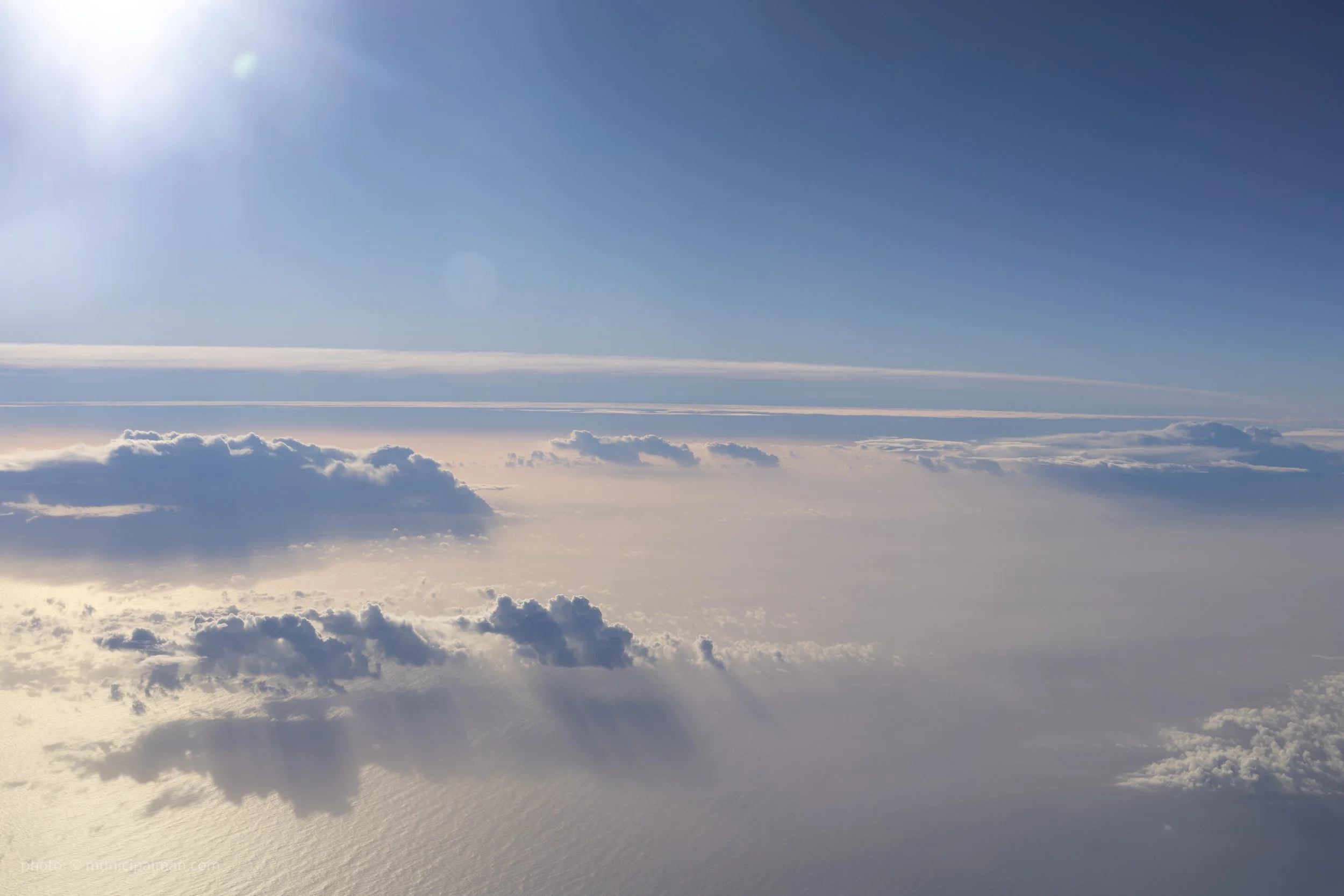 View of the sky and clouds taken from above, with sunlight shining from the upper left corner and a clear blue sky.