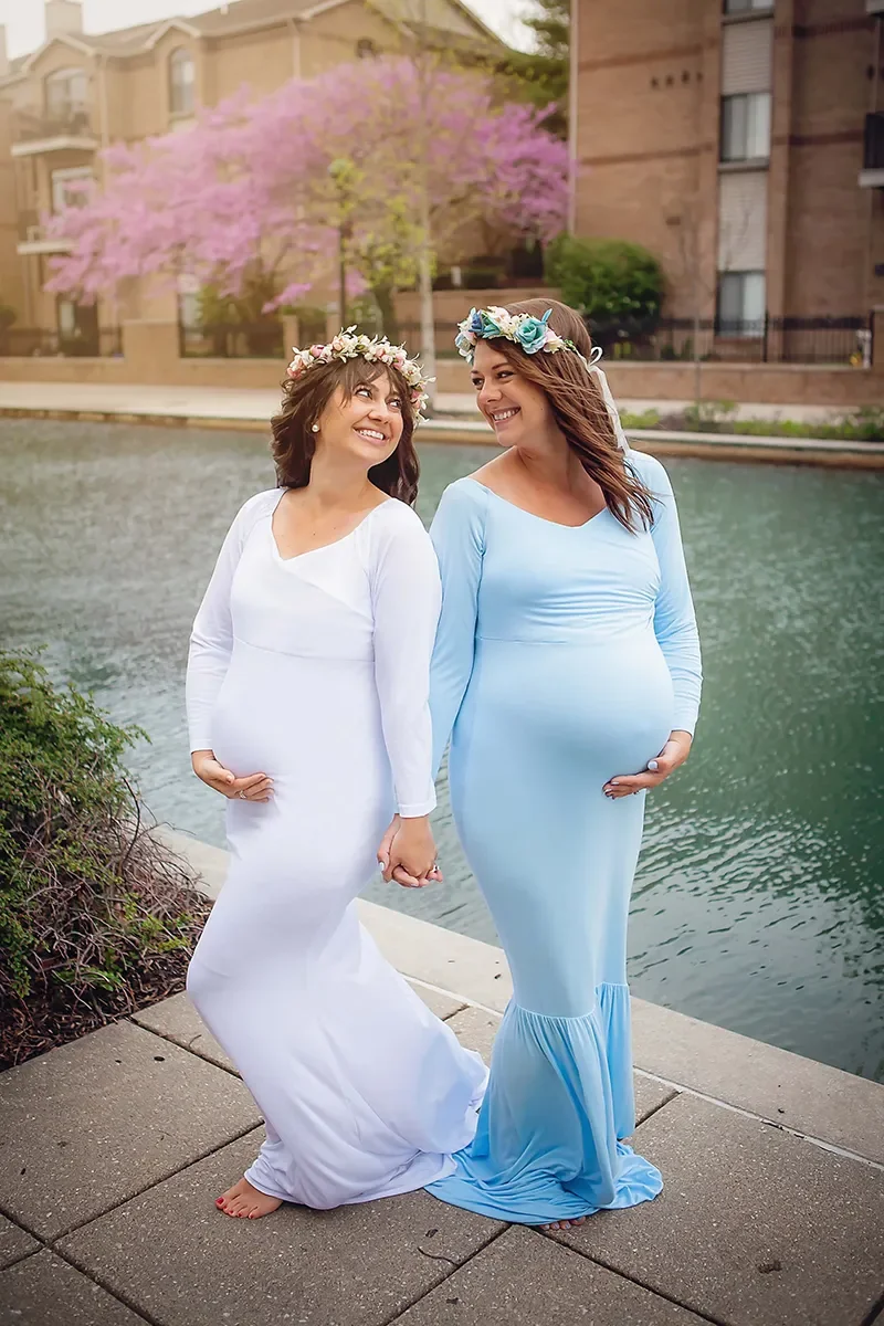 Two expectant mothers wearing floral crowns walk hand in hand during an outdoor maternity photography session in Indianapolis