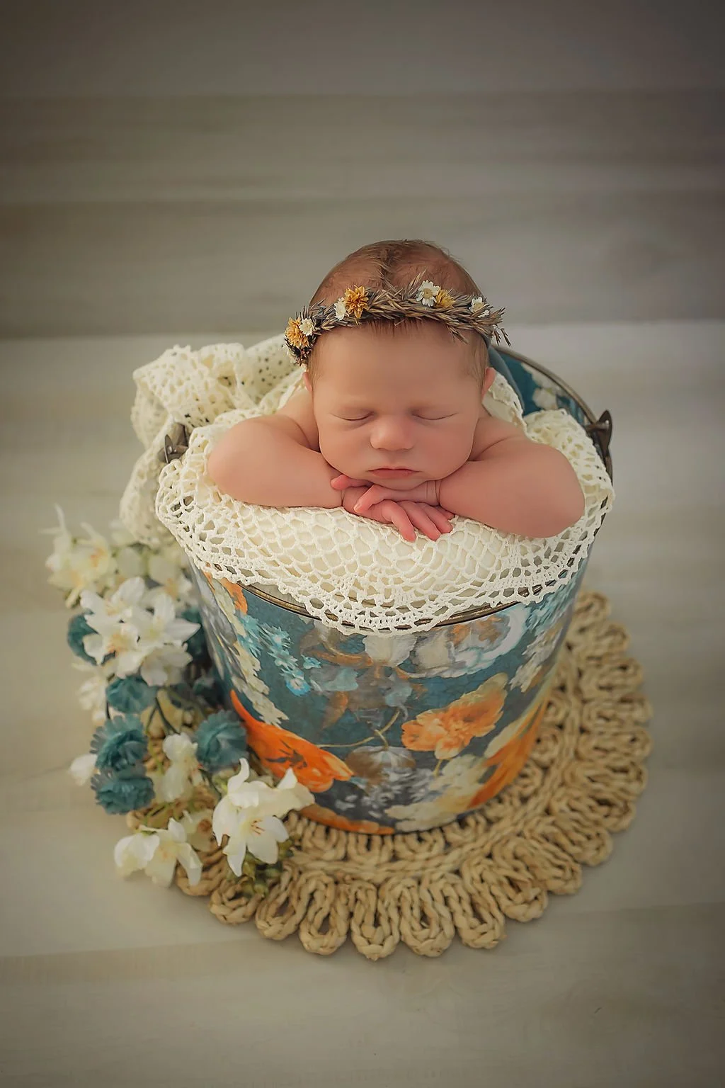 Baby girl sleeping with her hands rested on the edge of a floral bucket with lace and flowers surrounding her during her newborn photography session in Indianapolis.