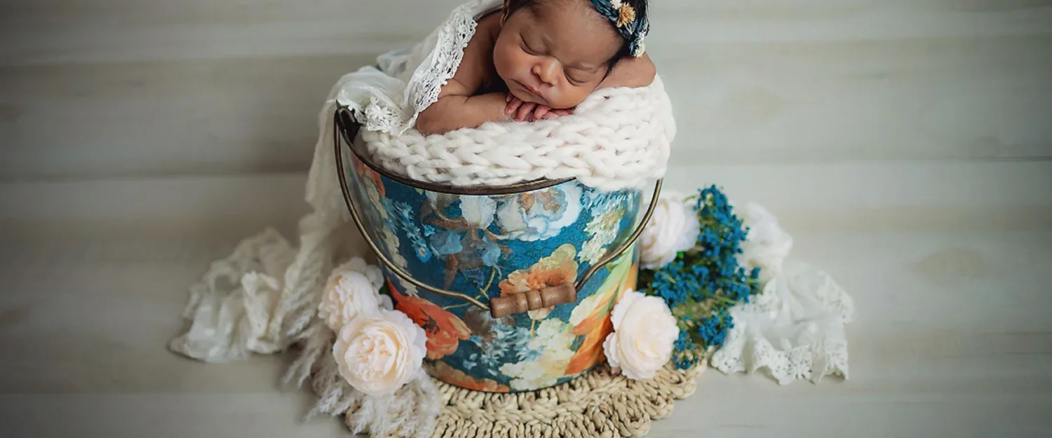 Newborn baby girl snuggled in floral bucket with lace wrap and blanket wearing a floral headband taken by Memory Lane Photography Indianapolis.