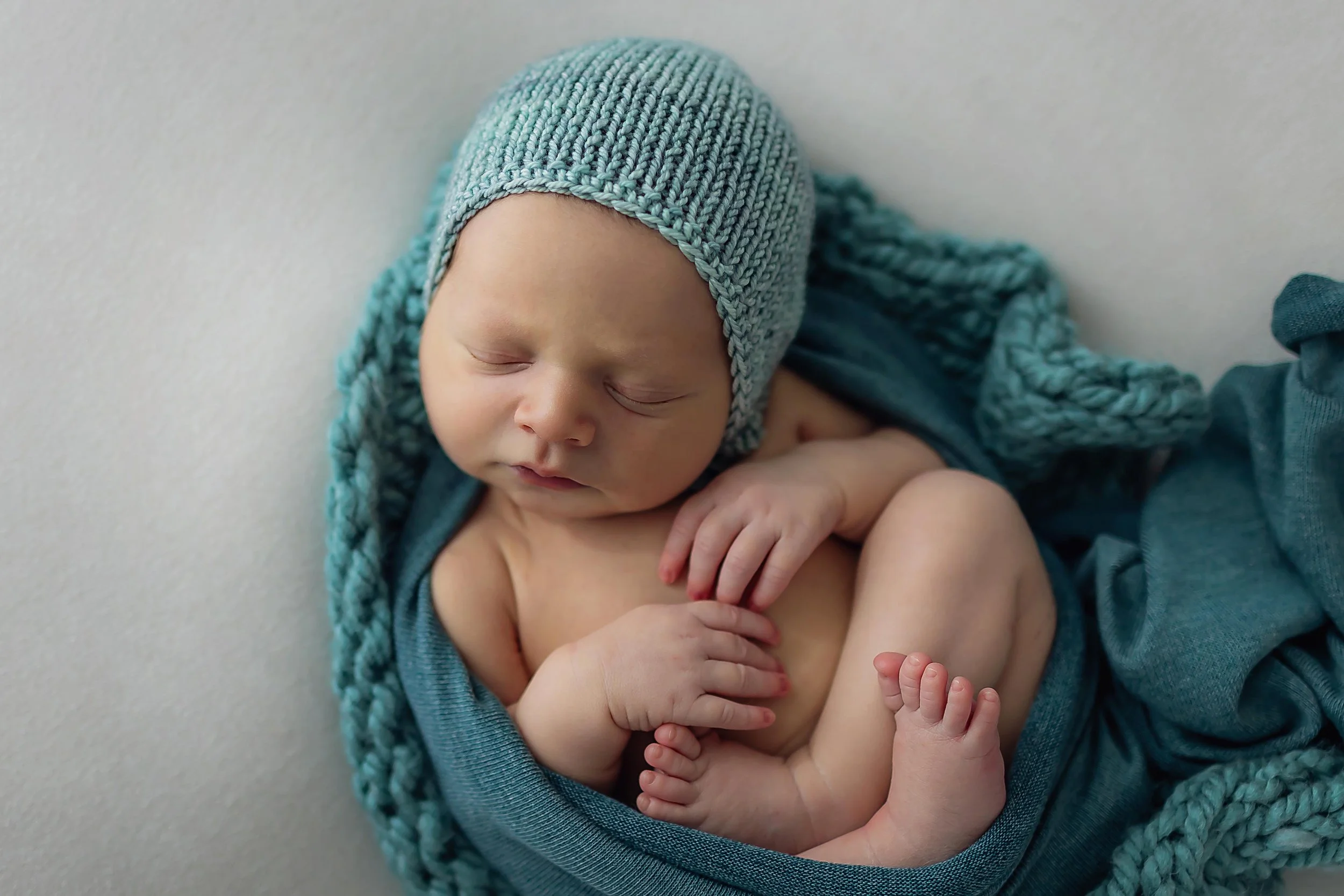 Newborn baby boy with robin blue bonnet posed on matching colored wrap