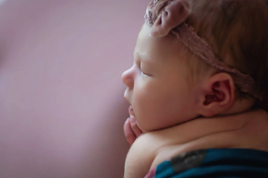 Close-up on baby girl during a newborn photography session in Indianapolis sleeping on a mauve background showing her sweet face laying on her hand.