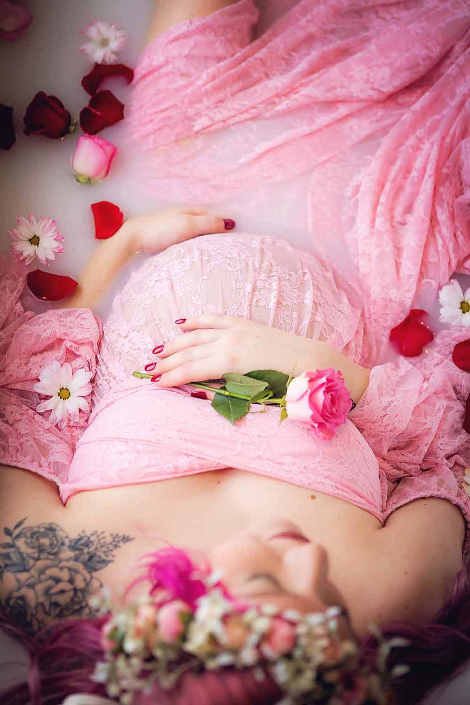 Expecting mother in pink maternity dress holding a single pink rose while enjoying a milk bath maternity session.