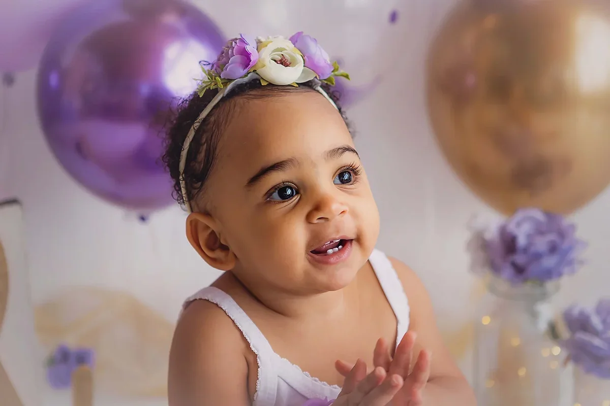 Baby smiling during a milestone portrait session with pastel balloons and floral accents in a photography studio