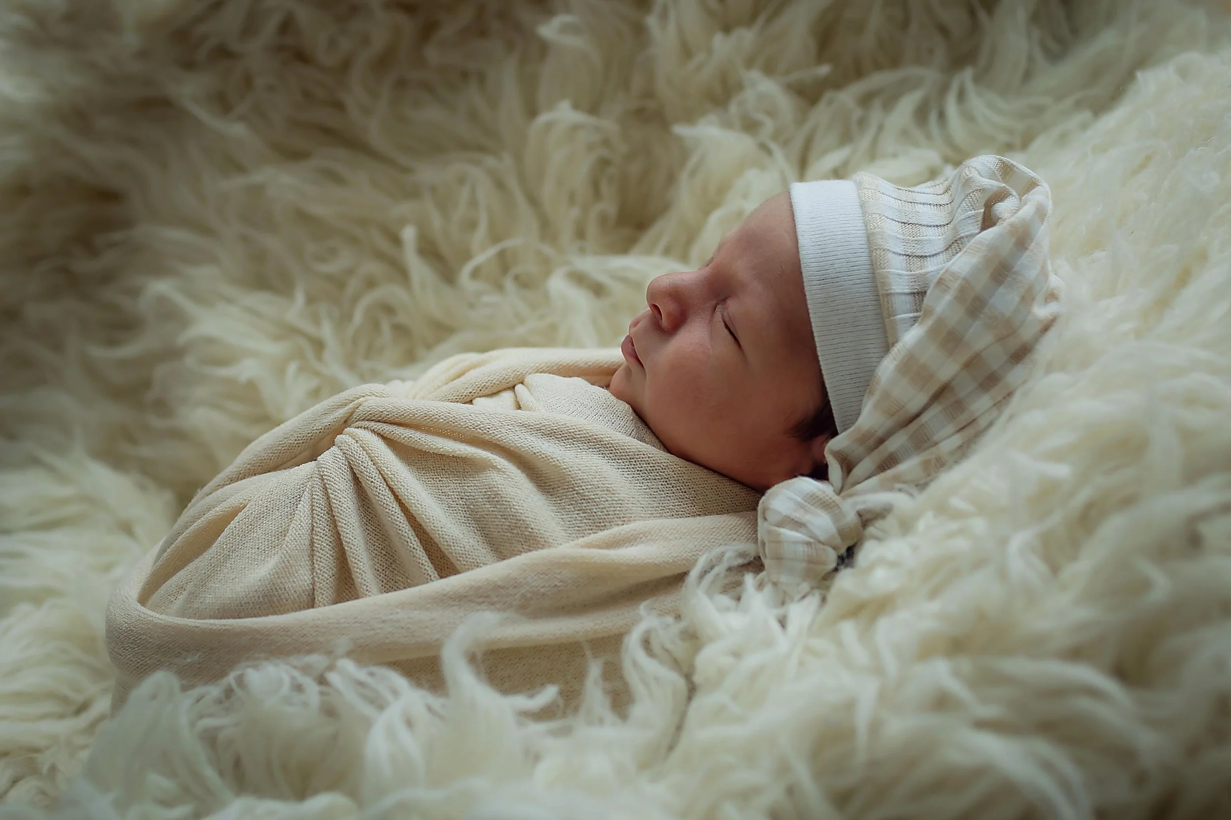 Newborn baby boy posed in cream with striped khaki and white sleeping cap in Indianapolis studio