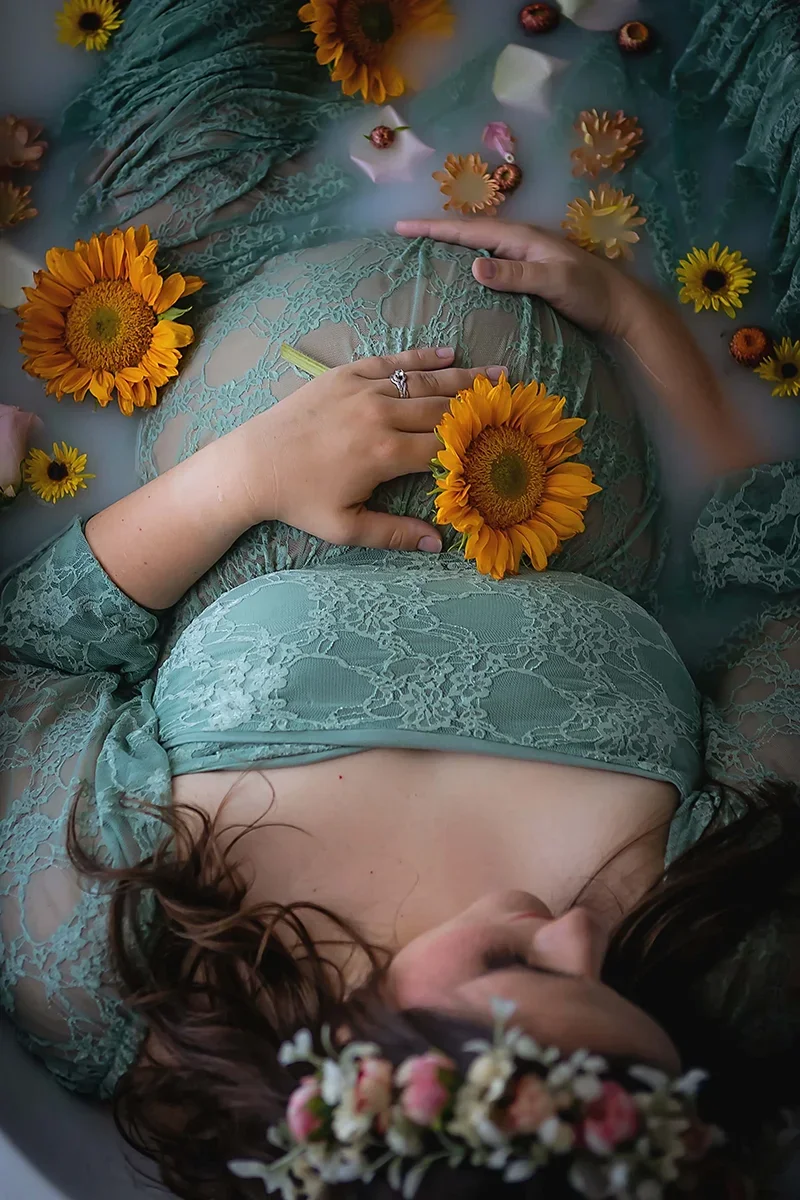 Pregnant woman laying in a luxurious milk bath wearing a sage lace gown during a maternity session in Indianapolis