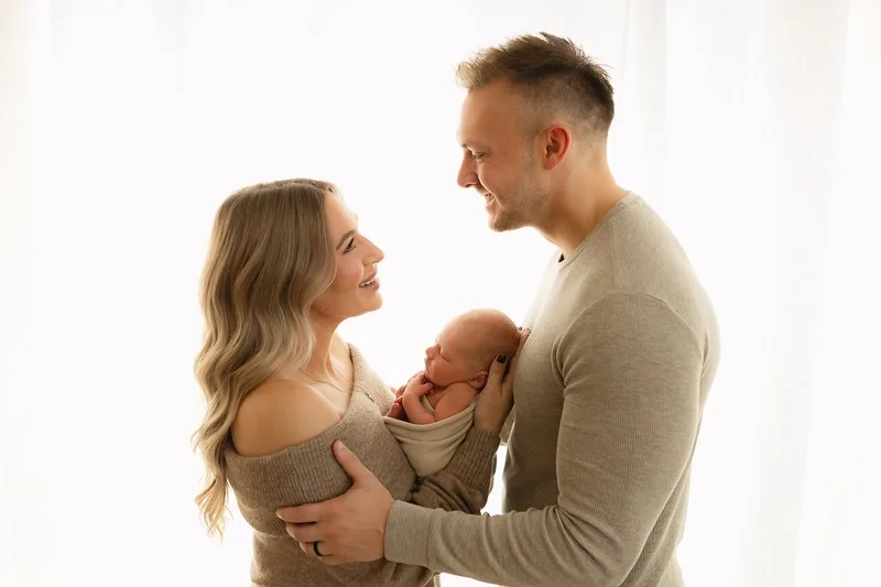 Mother and Father looking into each other's eyes with newborn baby snuggled up between them at Indianapolis studio