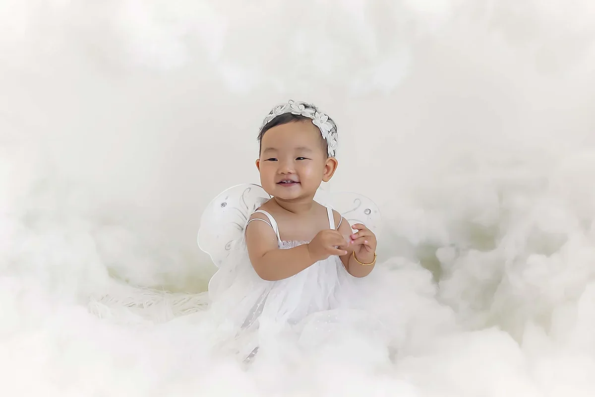 One-year-old baby in a white dress with delicate wings, photographed in a soft, ethereal studio setup for a milestone session in Indianapolis