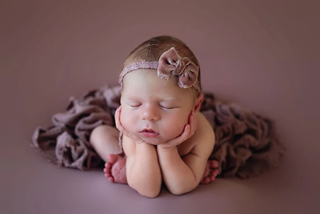 Indianapolis newborn photographer session with a baby girl in "froggy" pose wearing a velvet bow on a mauve background.
