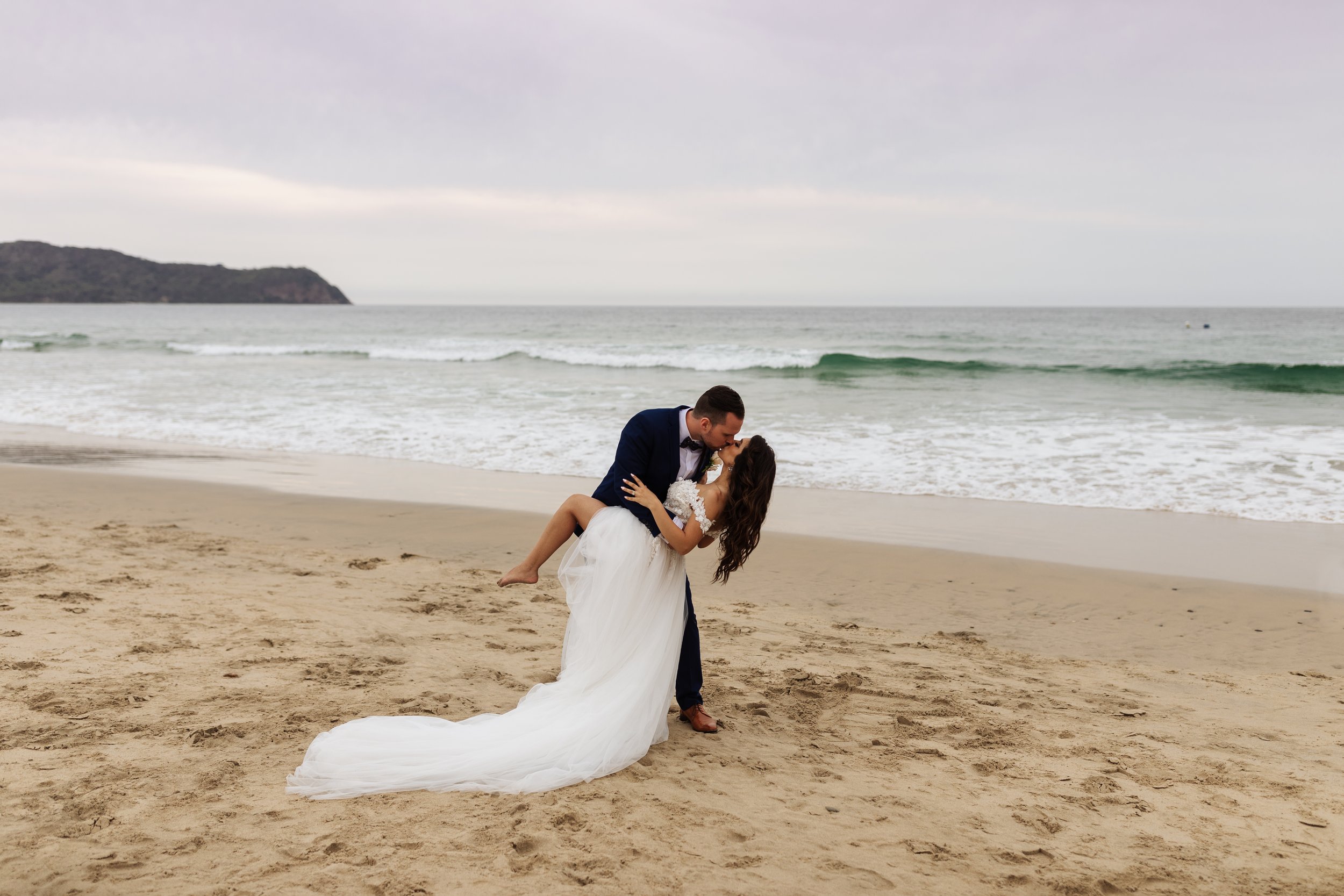 Couple in wedding attire kissing on a beach.