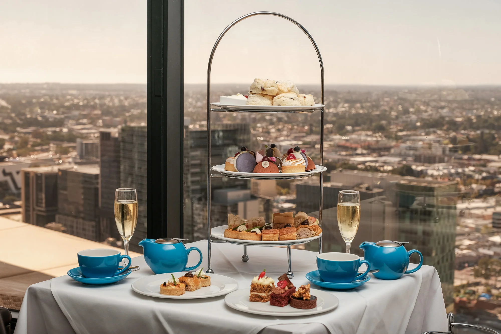Three-tier high tea with scones, cakes and savoury treats with two glasses of bubbly overlooking Perth