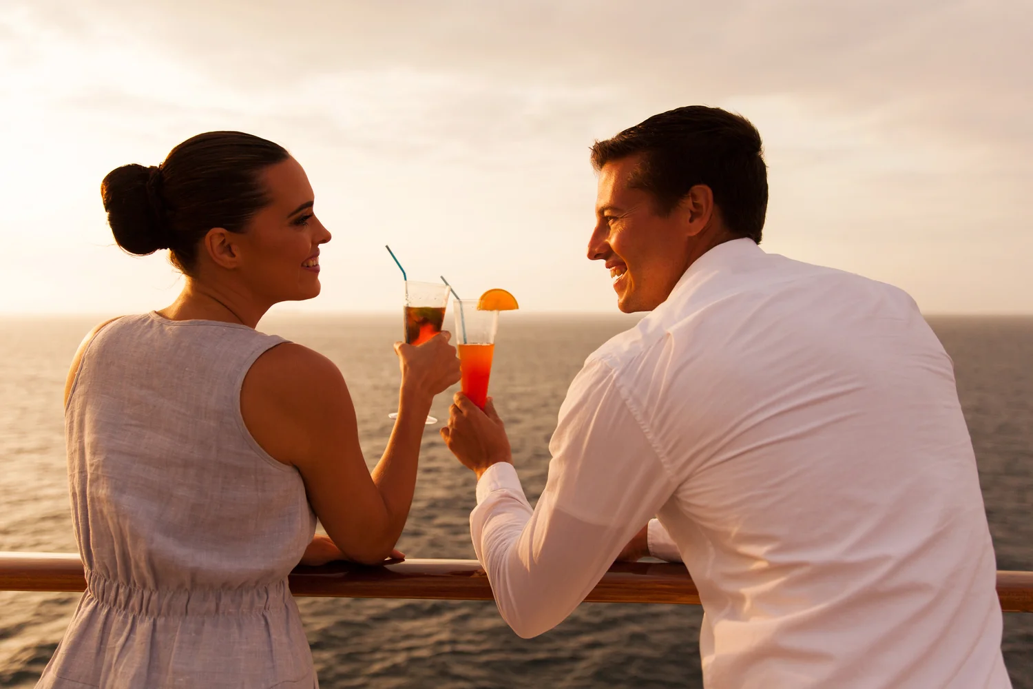 Young couple clinking cocktail glasses while overlooking the ocean onboard a cruise ship