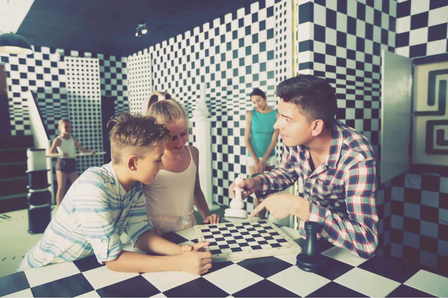 Young family huddled over a chessboard in a black and white escape room, trying to solve a puzzle