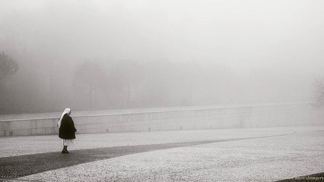 Nun walks back home after the mass surrounded by a mid afternoon blanket  of fog.