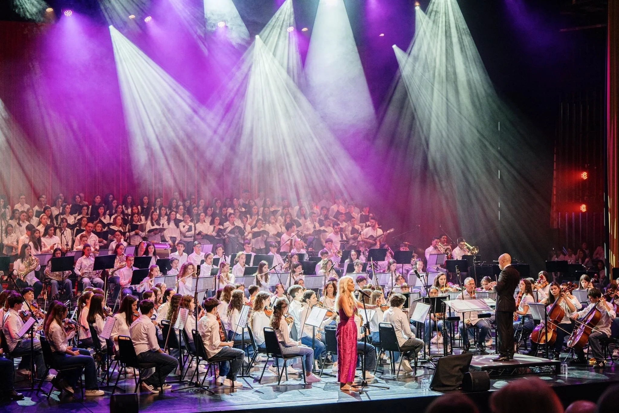 Orchestra and choir performing on stage with colorful stage lighting
