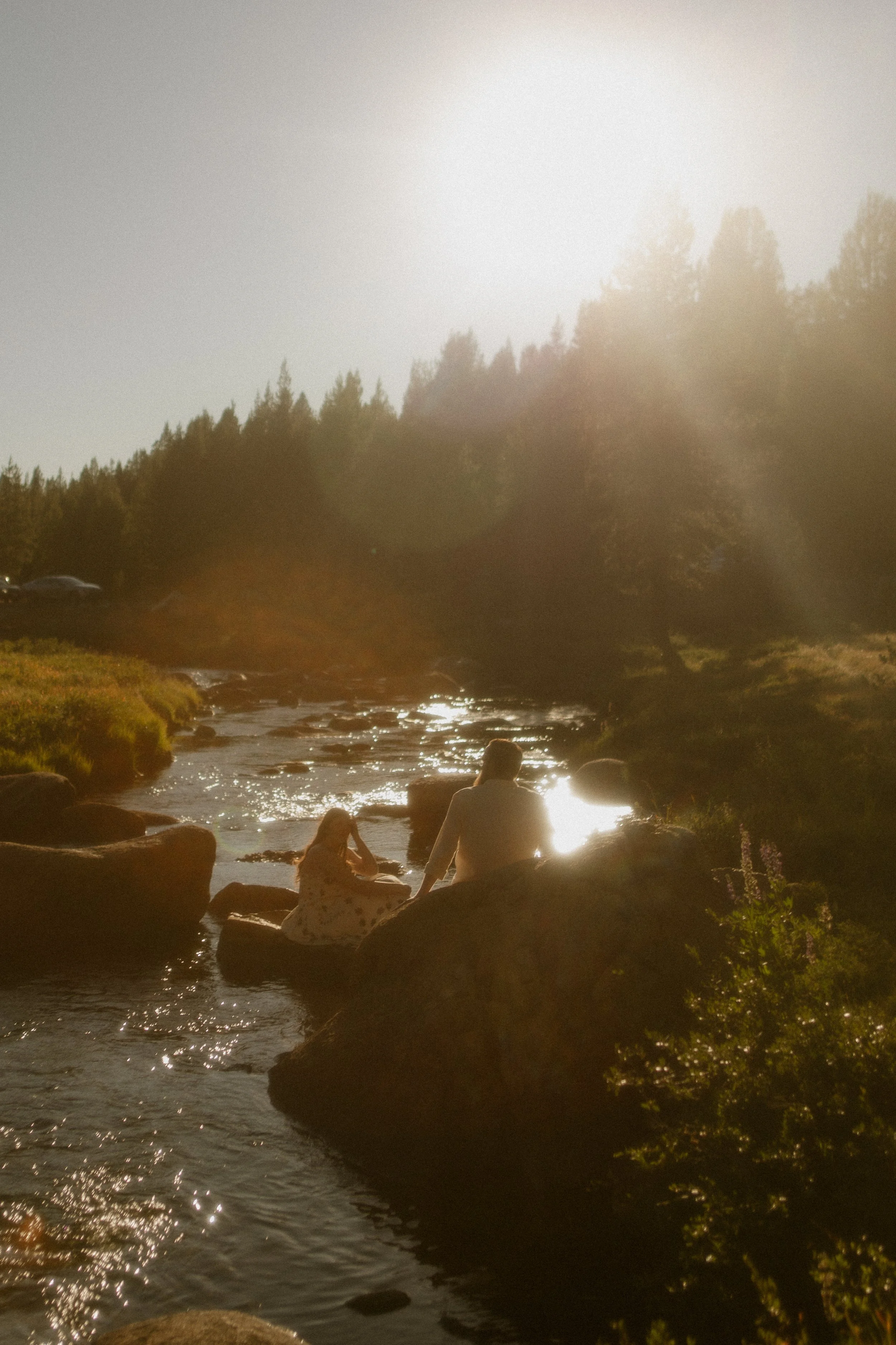 couple sitting on rocks in river in tuolomne