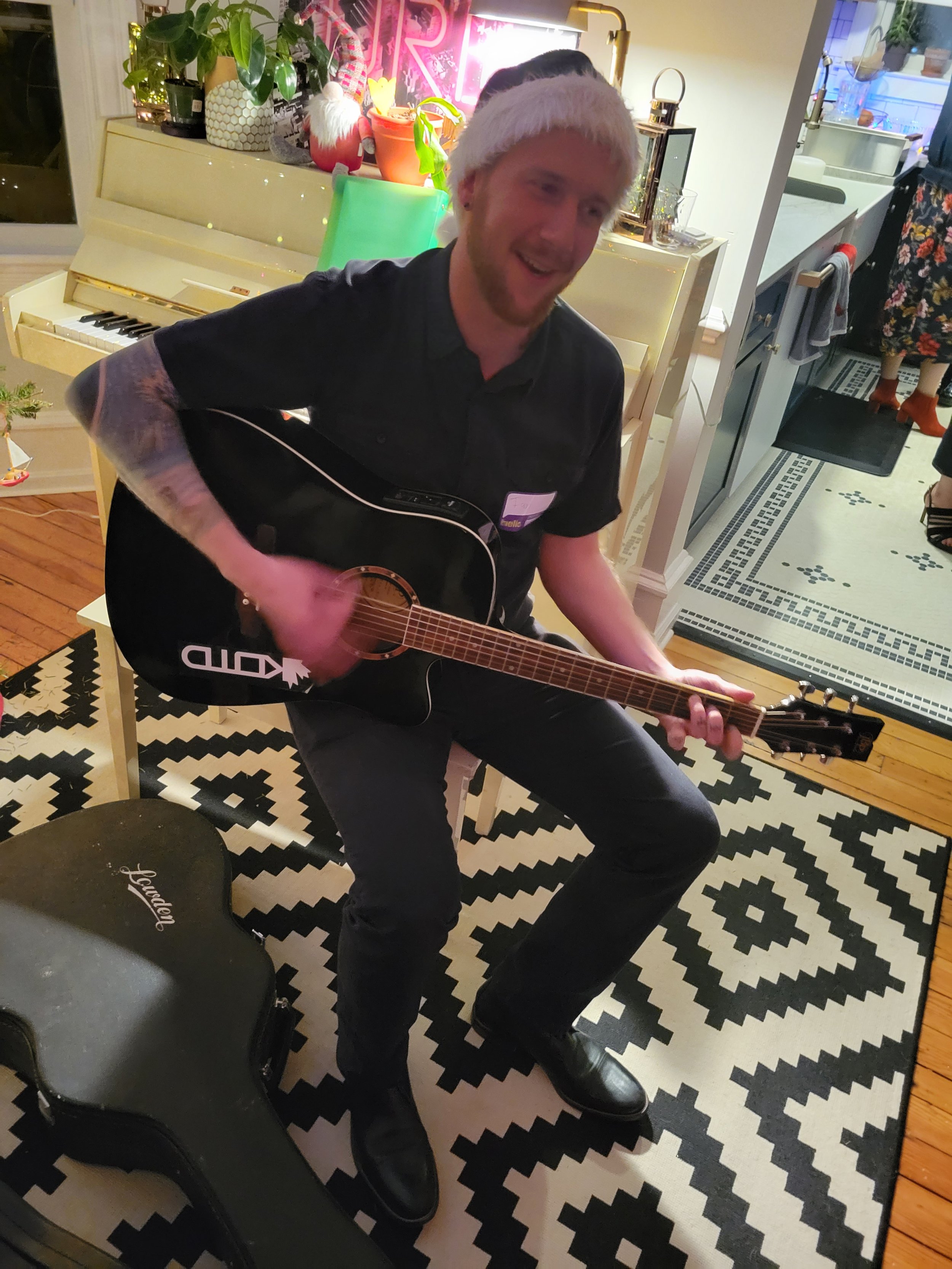    Vocal percussionist and bass, Ian, playing guitar for an instrument accompanied number at a private Christmas party Noteworthy performed at in 2022.   