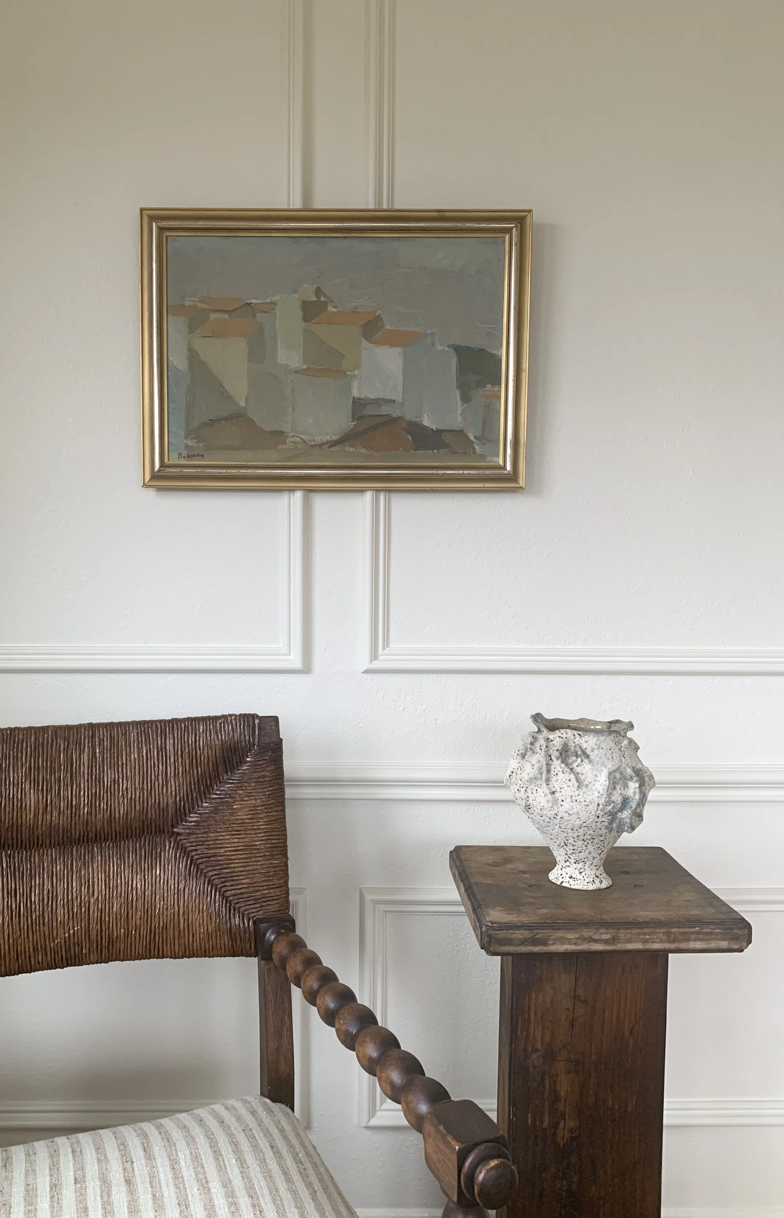 ‘Spanish Village in Summer’ (ca. 1960s), hanging on wall above a vase and chair.