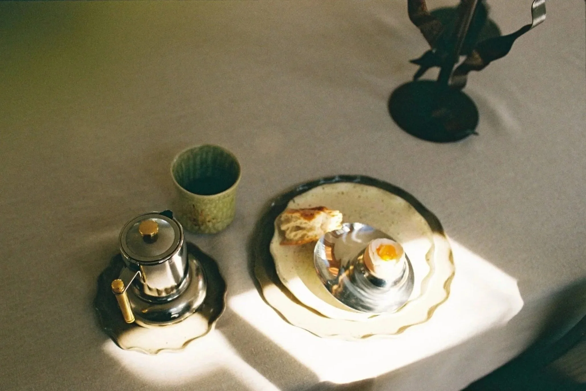 Sunlit table scene featuring handbuilt Ruby Bell Studio ceramic plates, a small teapot, and a simple breakfast—an intimate study in collected design objects that celebrate craftsmanship and timeless everyday rituals.
