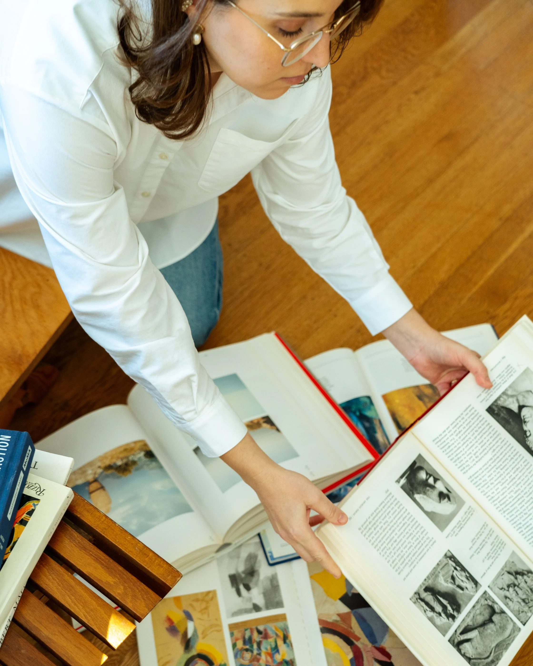 Artist reviewing open art books spread across a wood floor, referencing visual research and inspiration.