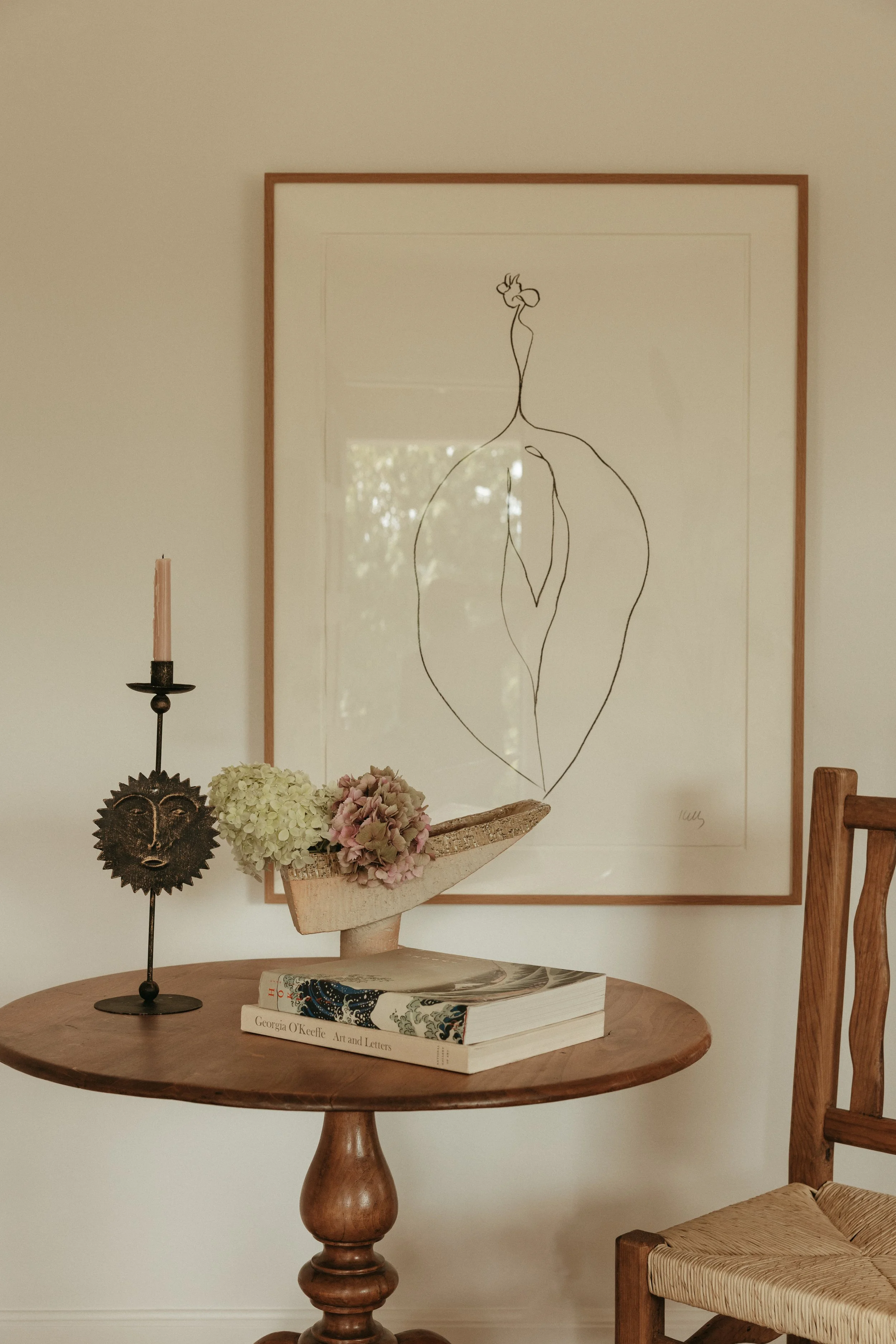 Thoughtfully curated vignette with an Ellsworth Kelly lithograph, vintage candle holder, hydrangeas in a handmade vessel, and art books—reflecting a home filled with modern heirlooms.