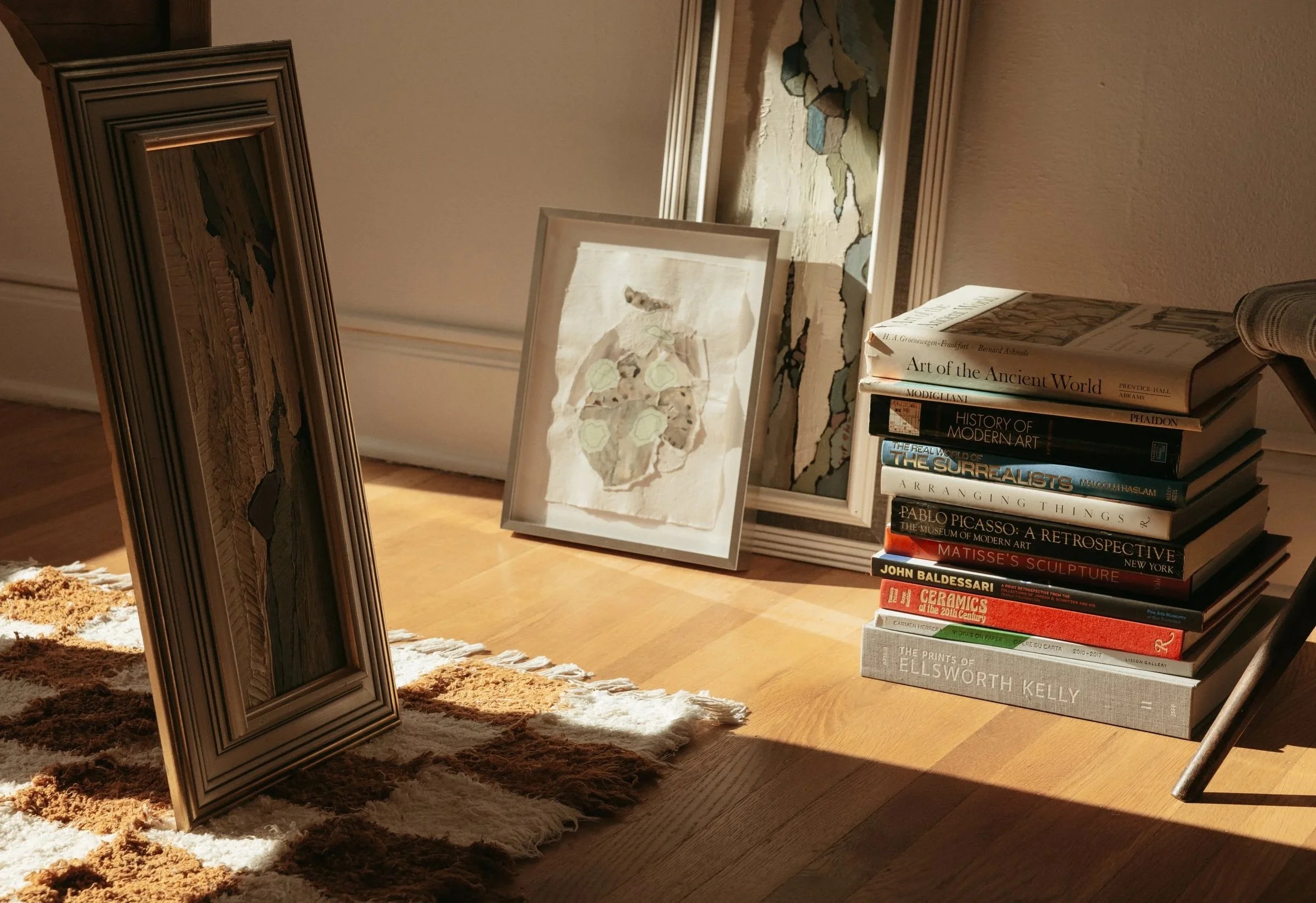 Framed artworks and art books gathered in a sunlit interior, evoking the intentional, collected process behind Ruby Bell Studio’s bespoke art and design sourcing.