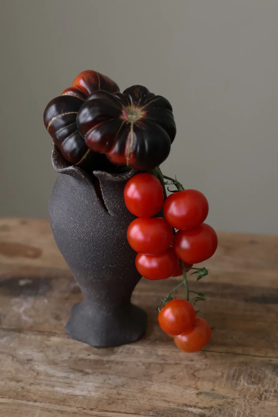 Handbuilt sculptural Ruby Bell Studio vase with undulating edges arranged as a still life on a wood table.