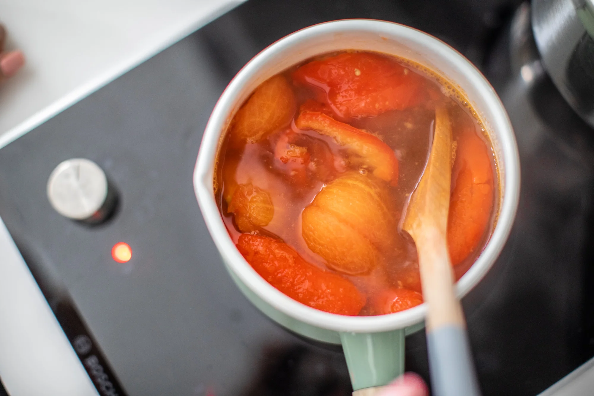 Add chicken broth, peeled tomatoes and peppers, garlic and white onion into pot. Simmer till soft.