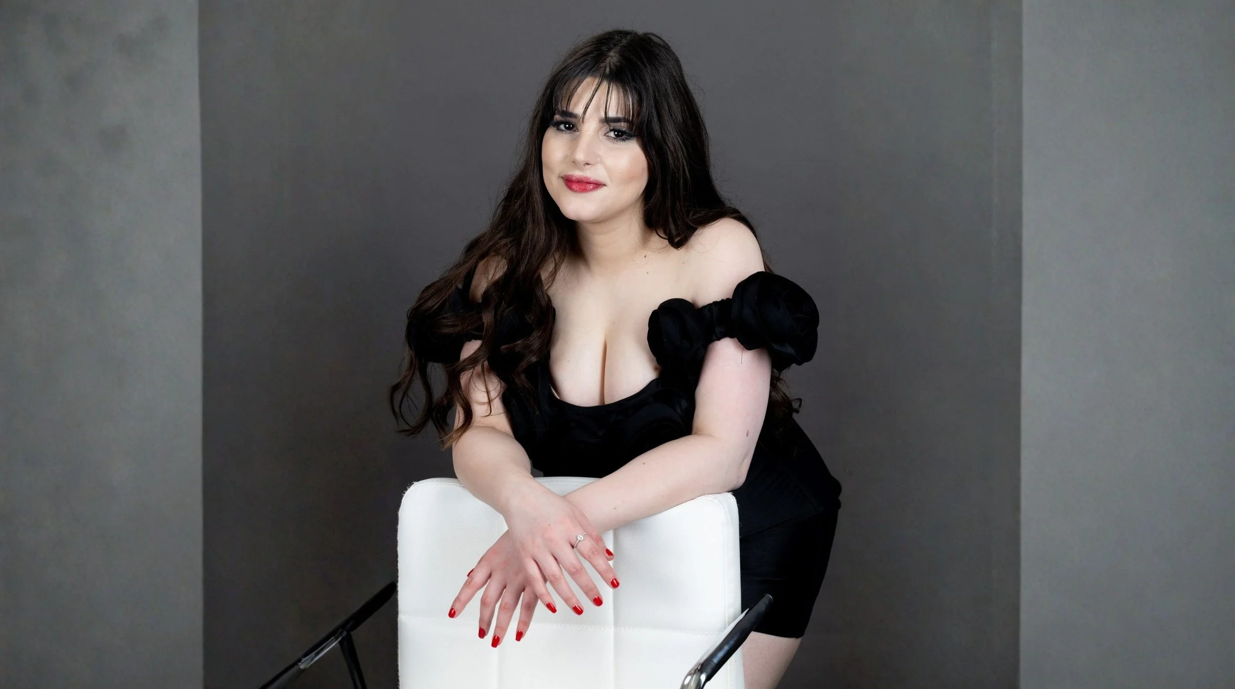 Beginner model leaning on chair with natural smile demonstrating relaxed pose in professional photoshoot setting