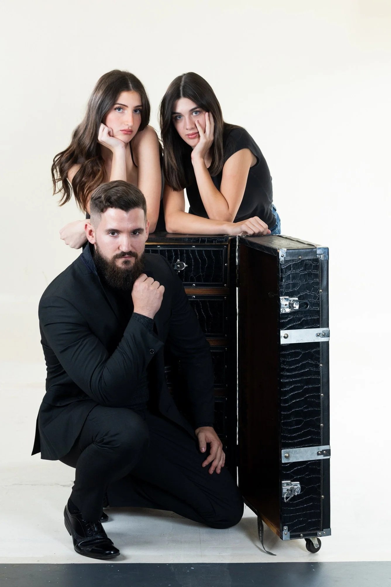 Studio portrait of three models posing with fashion props wearing black outfits in a minimal setting representing editorial and commercial modelling styles