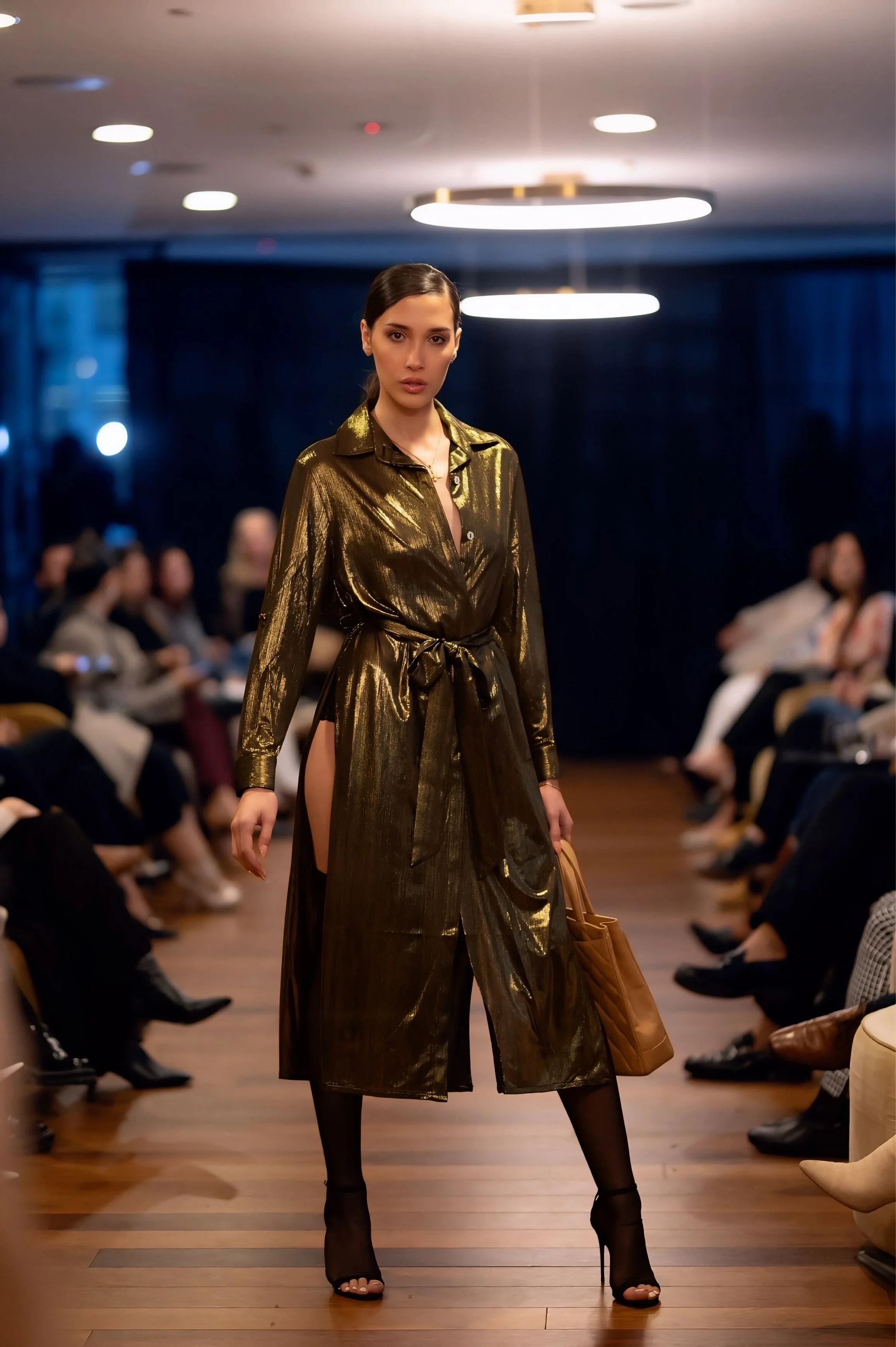 Fashion runway model walking confidently in a metallic gold dress during a live catwalk show, demonstrating professional runway posture and presence.