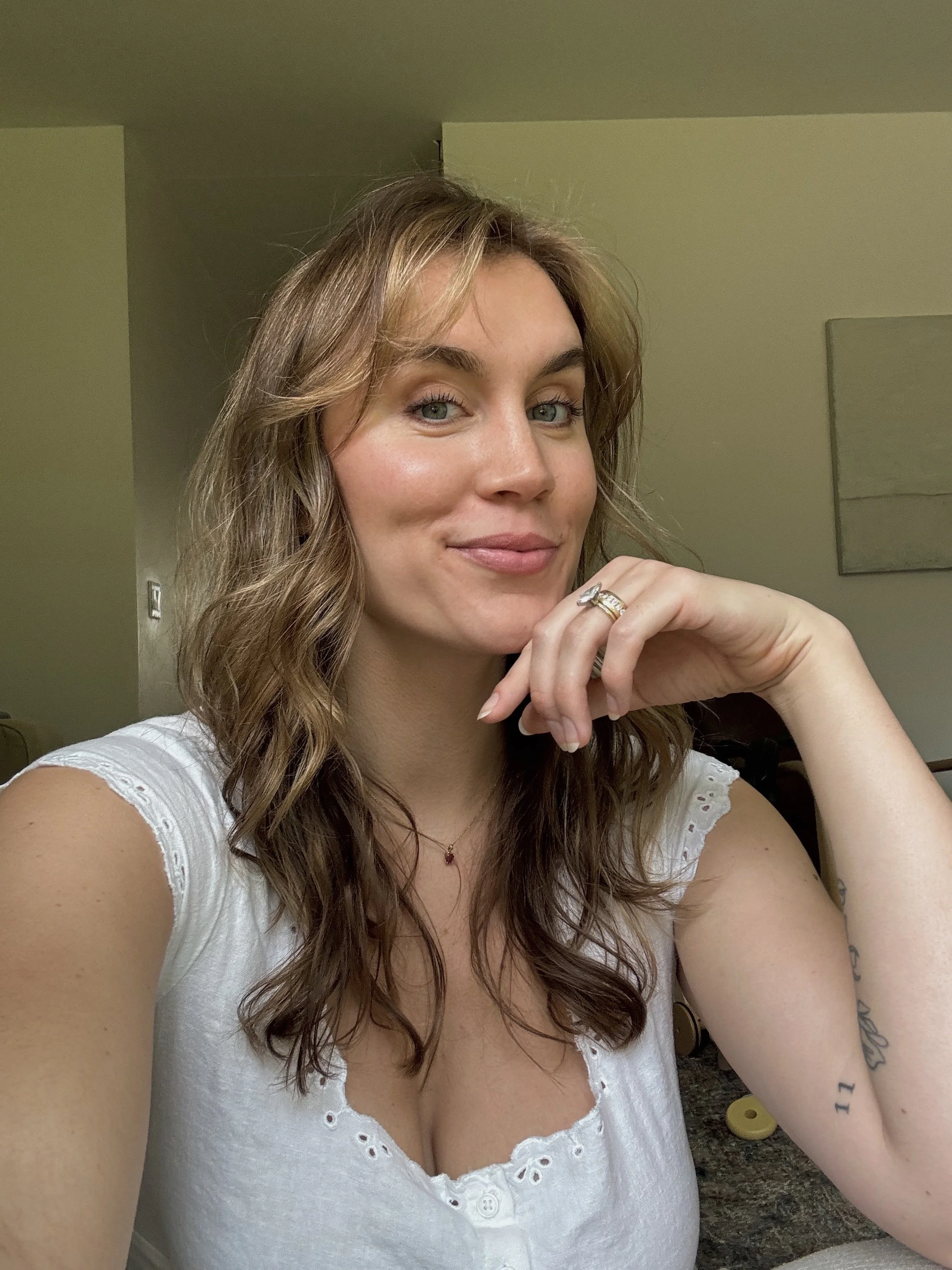 A woman with shoulder-length wavy blonde hair, wearing a black button-up sweater, smiling with her hand on her hip.