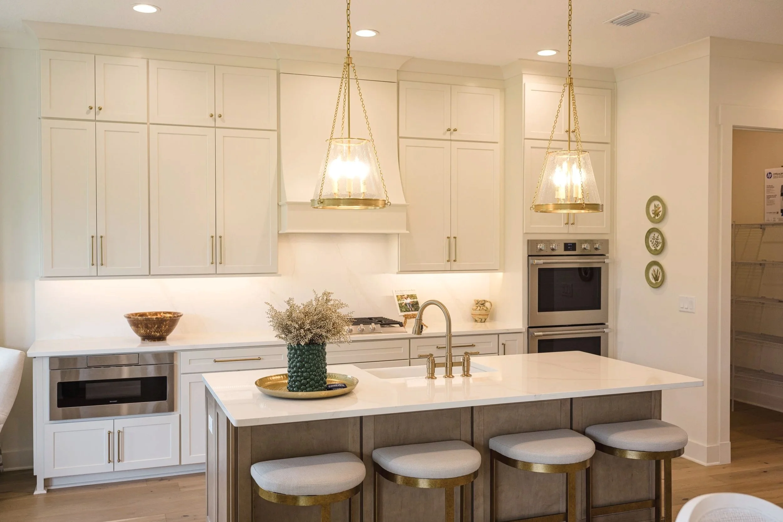 Modern white kitchen with gold accents, hanging pendant lights, and a kitchen island with four barstools.