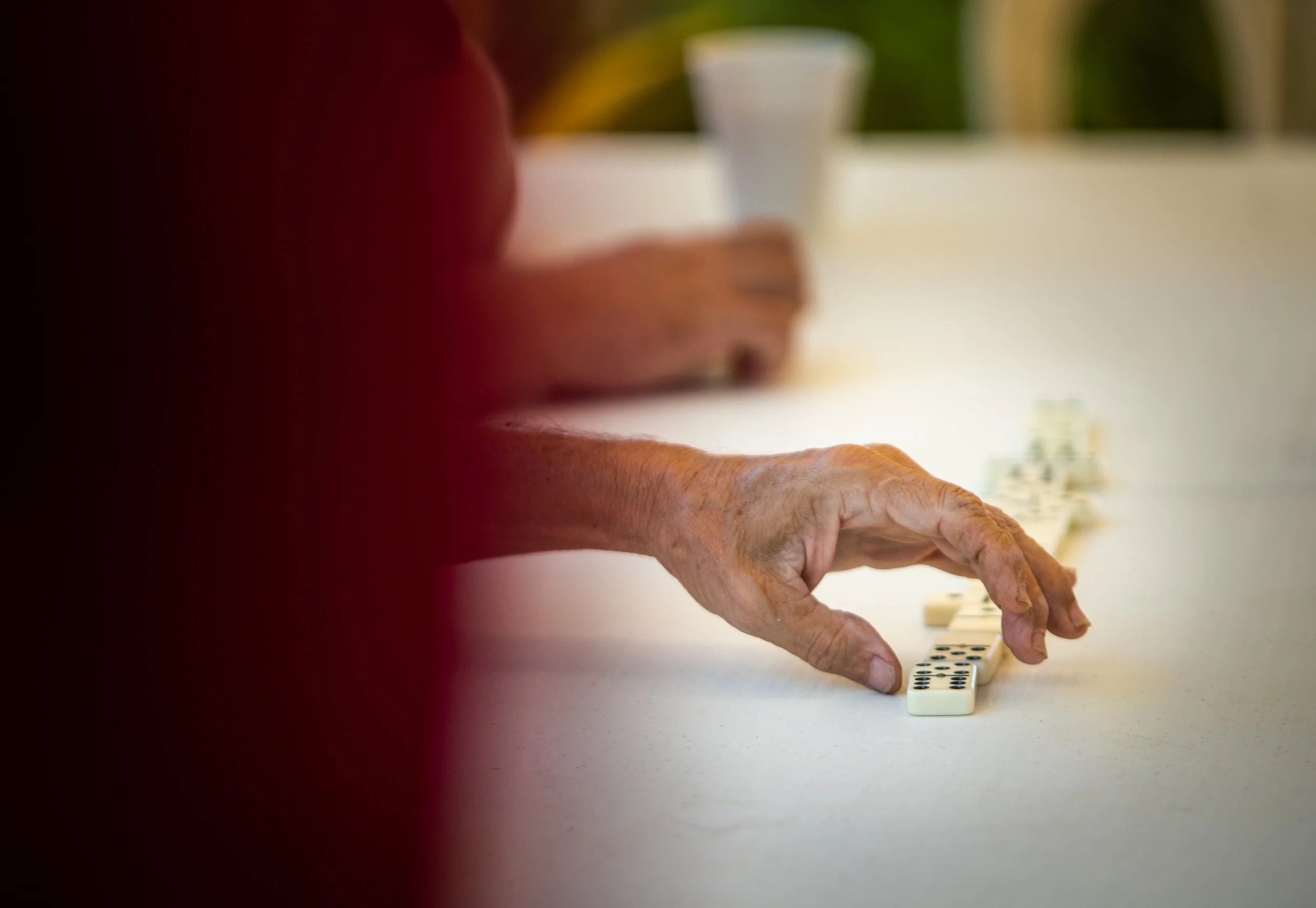 Persona mayor jugando dominó en una mesa. 