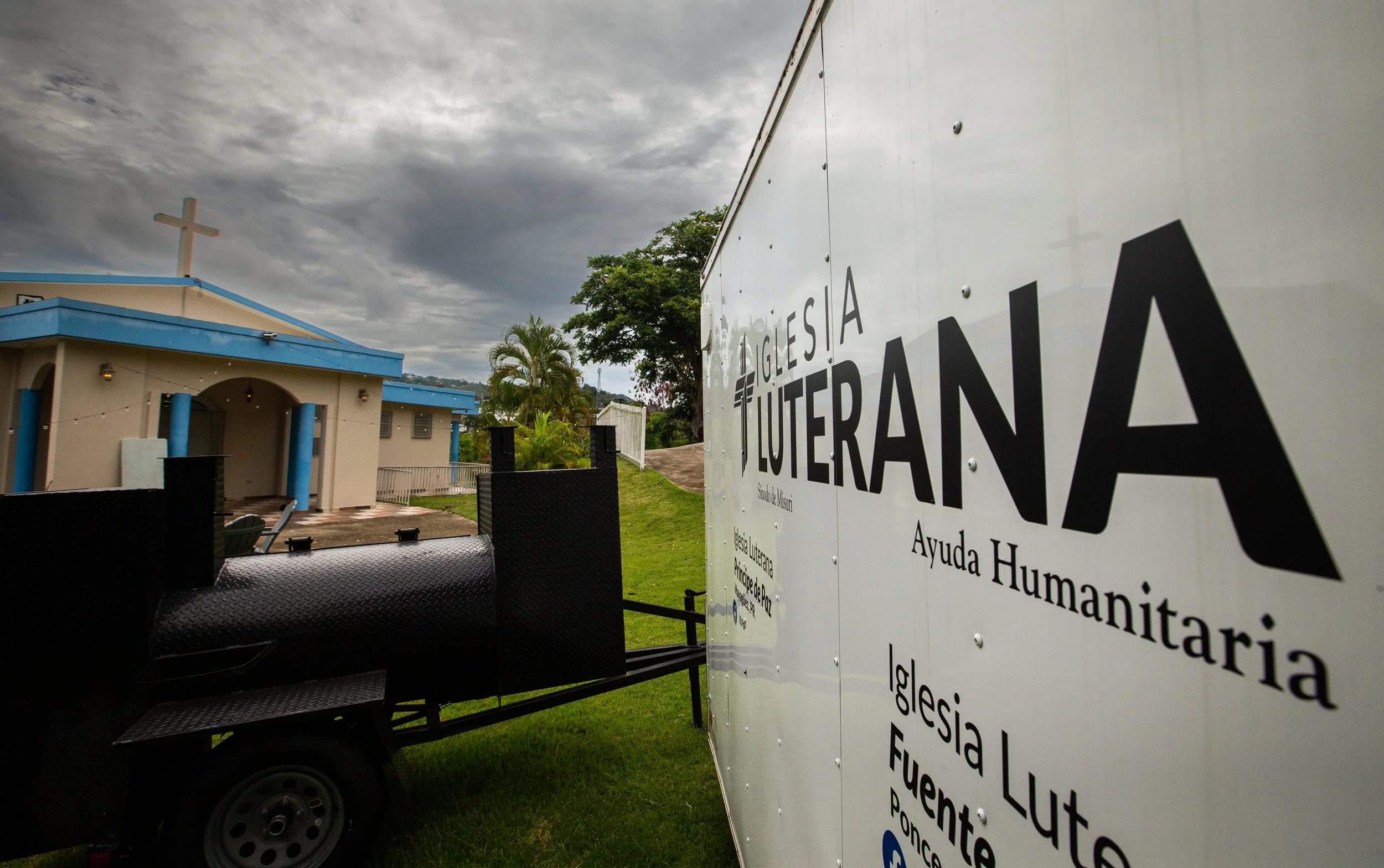 Camión de ayuda humanitaria de la iglesia luterana cerca de una iglesia con un cielo nublado.