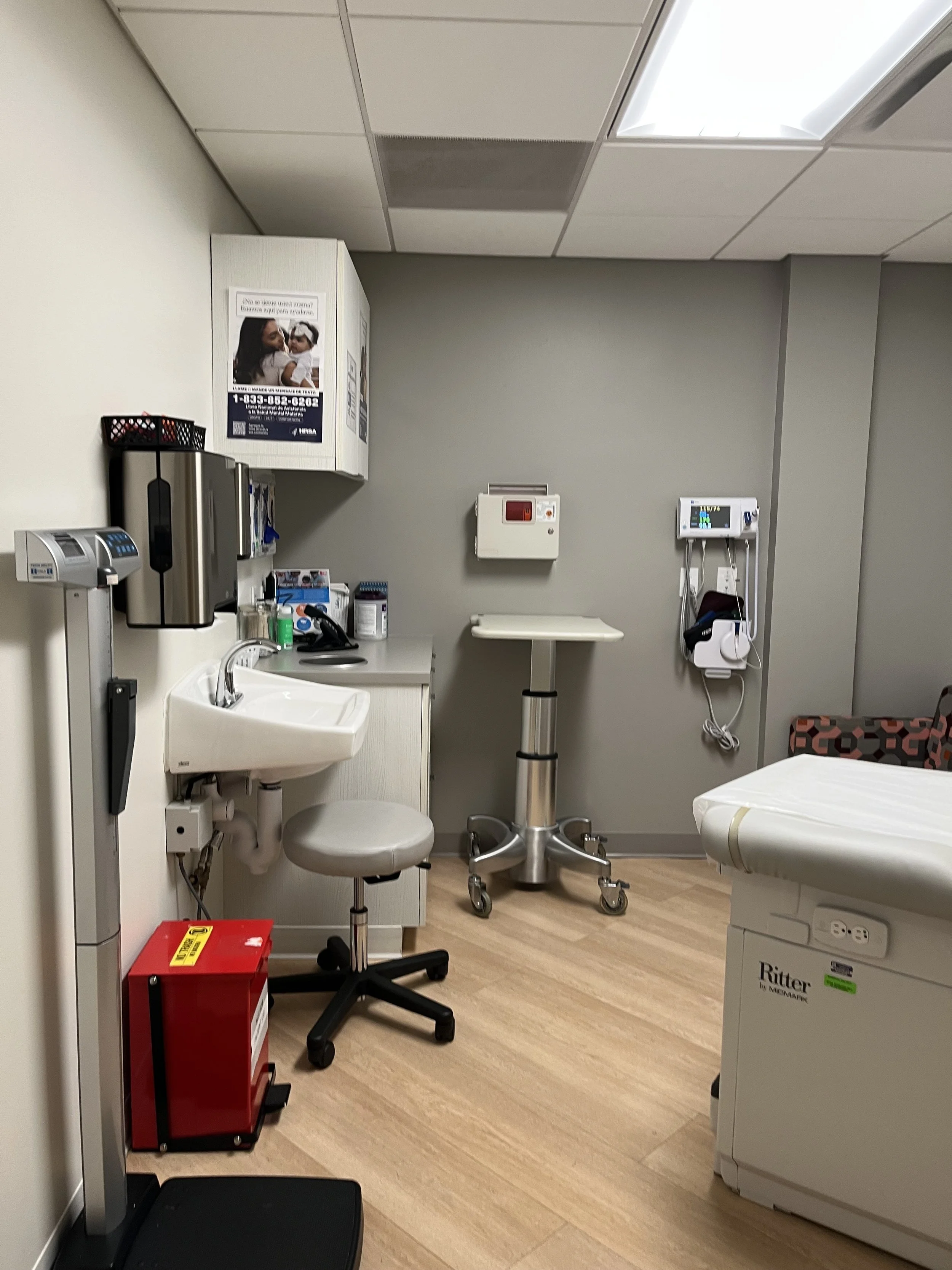 A doctor's office exam room showing a scale, sink, exam table, and other medical instruments.