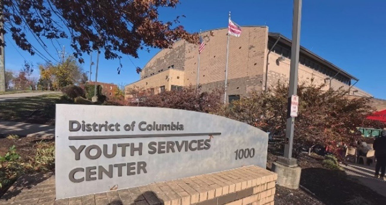 Exterior view of the District of Columbia Youth Services Center with a sign in the foreground and flags and a brick building in the background