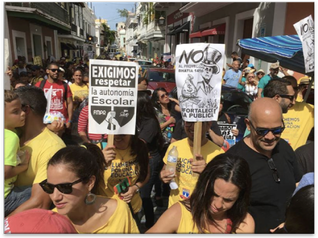 Puerto Rican educators march in the streets of Old San Juan protesting Project 1456, which allows the fast-tracking of school closures and the requirement to open new charter-type schools. Their signs read “We demand respect for school autonomy” and carry a sign of an imperial Uncle Sam.