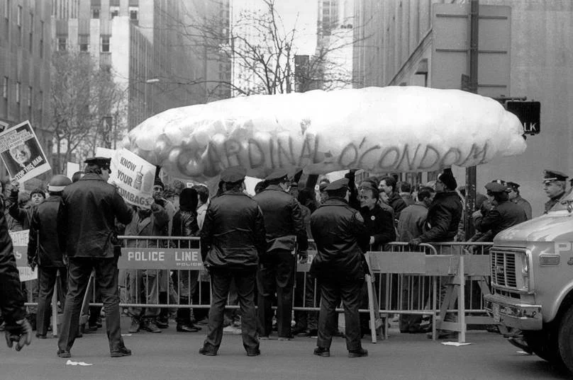 ACT UP and WHAM! members gather outside St. Patrick’s Cathedral during their “Stop the Church” action in December 1989. They protested Cardinal O’Connor’s opposition to condom use and to comprehensive sex education in New York City’s public schools. They also sought to raise awareness of the significant influence the Catholic Church wielded over the provision of health care for People with AIDS and the public funding it received for this purpose. ©Stacy Walsh Rosenstock