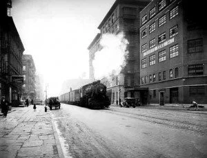 Freight train rumbling though Hell's Kitchen as children play on sidewalk