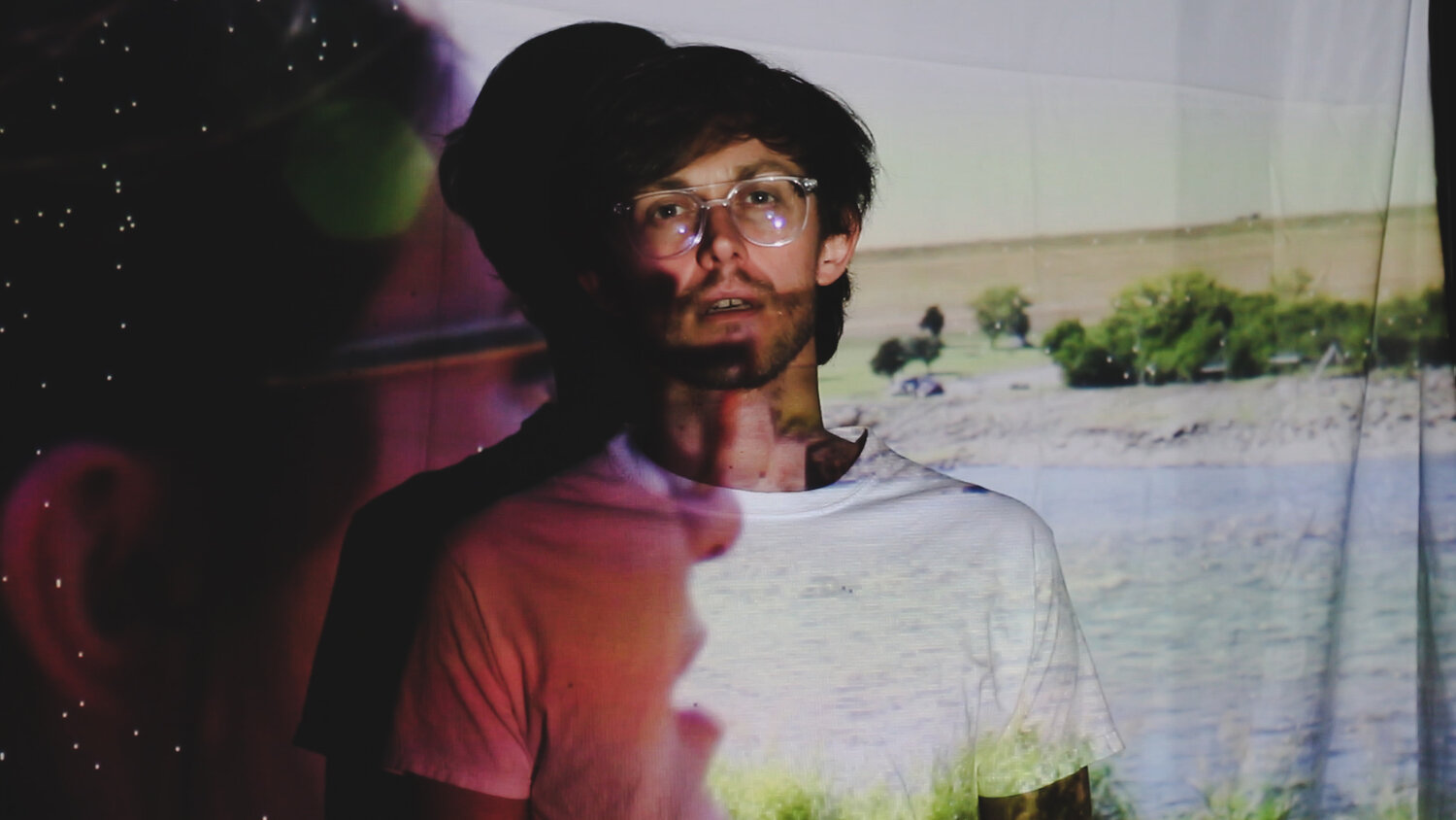Jordan Sutton of Goosechase wears glasses and stands in front of a sheet with a projected image of a deserted field.