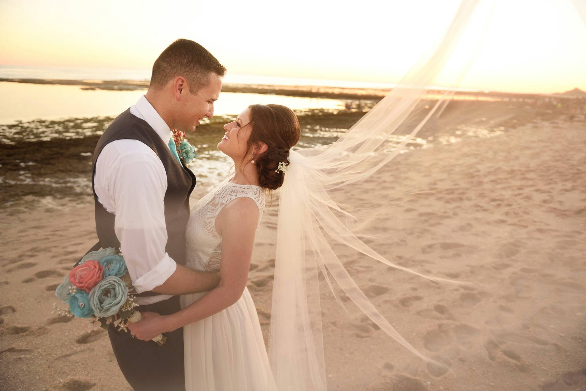 Bride and groom holding each other in bespoke lace wedding dress at beach resort wedding and long wedding veil.jpg