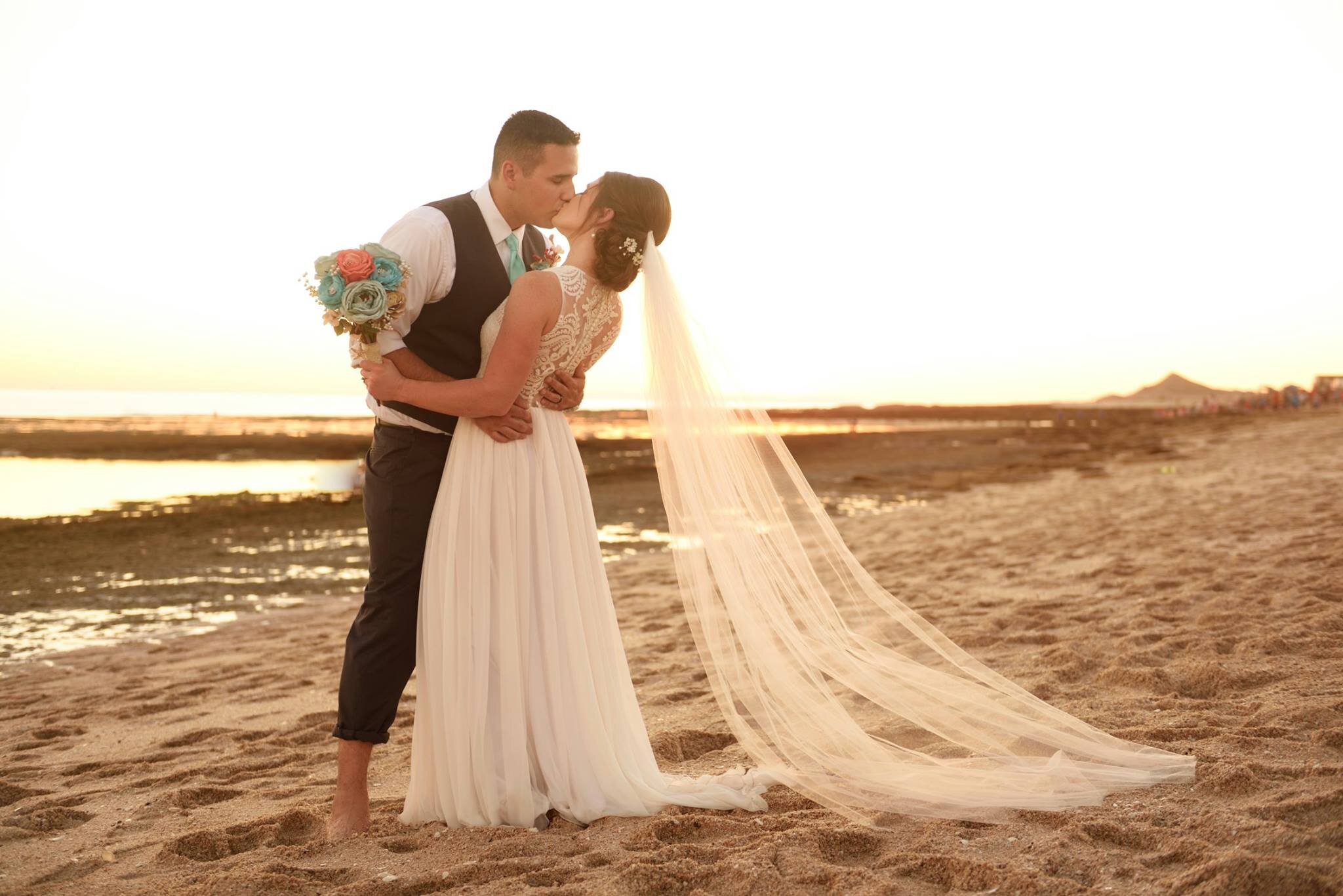 Bride and groom kissing at the beach wedding wearing bohemian lace custom made bridal gown with long veil.jpg