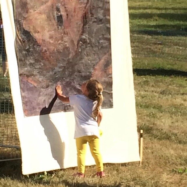   Yes, please touch.  A little girl has a close encounter with one of the Stations of the Cross painted by Gay Cox and arranged slalom-like on the ski slope location of SoulFest summer music festival in the mountains of New Hampshire. The Studio has 