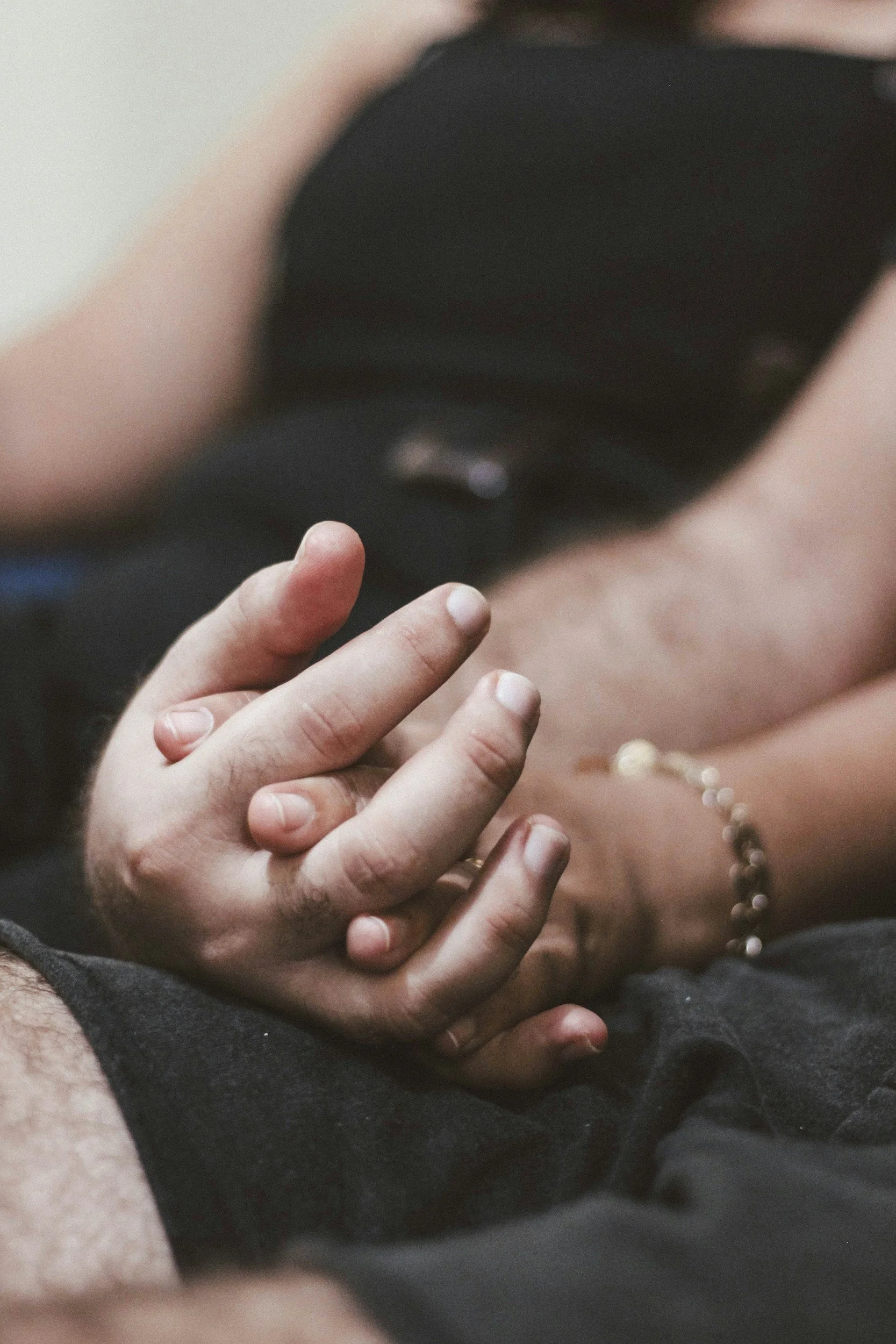 Close-up of two people holding hands, one with a gold bracelet, the other with a ring, with a smart watch in the background.