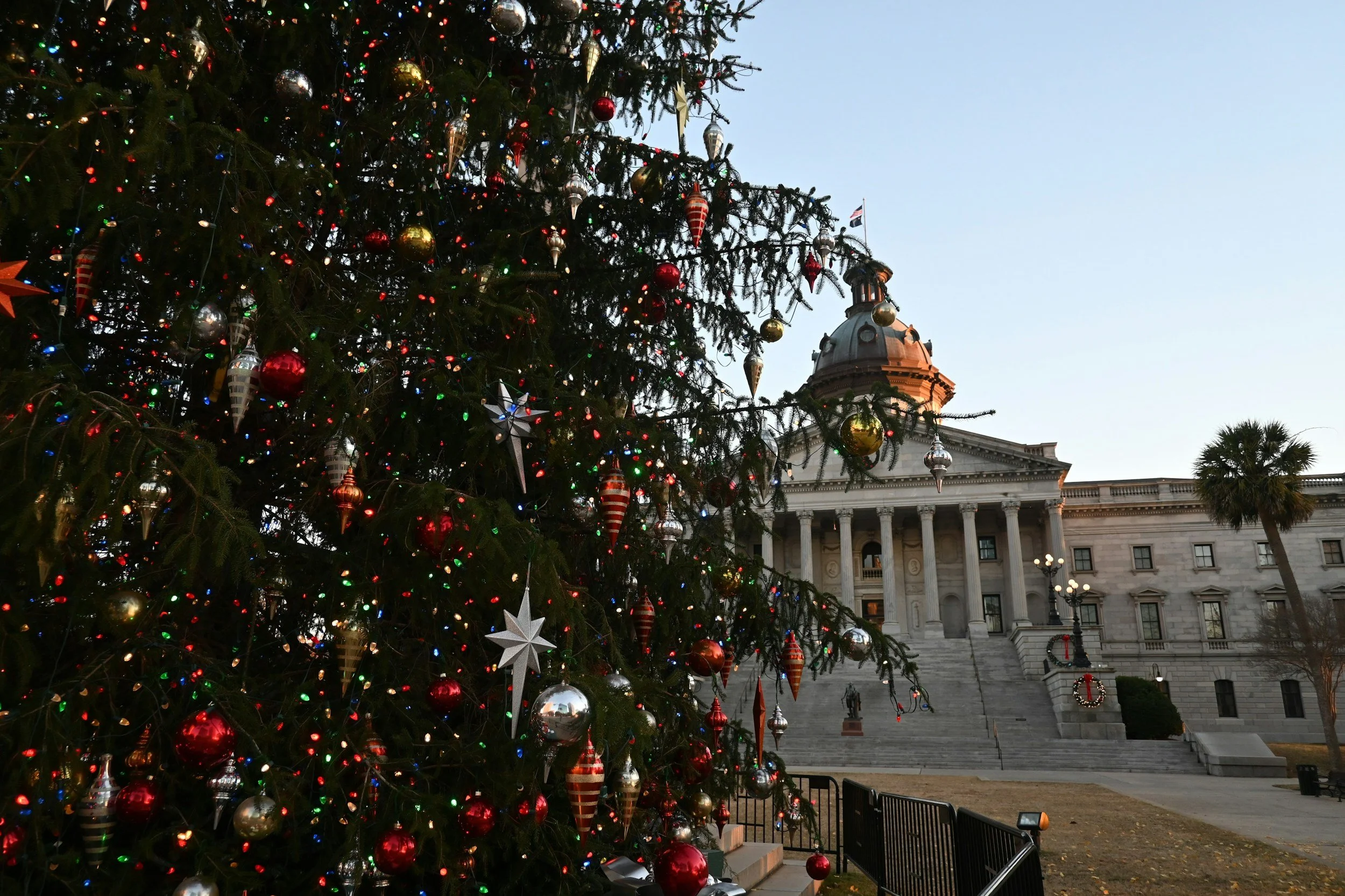 A decorated Christmas tree with red, gold, and silver ornaments in front of a government building with columns, a dome, and an American flag.