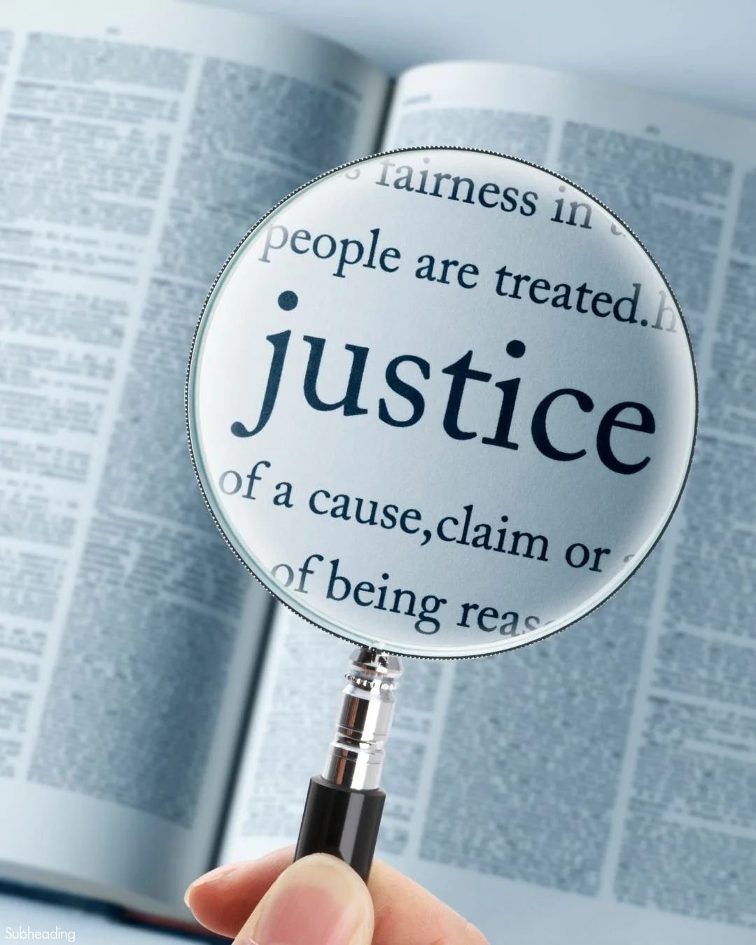 Magnifying glass focusing on the word 'justice' in a dictionary, with an open dictionary in the background.
