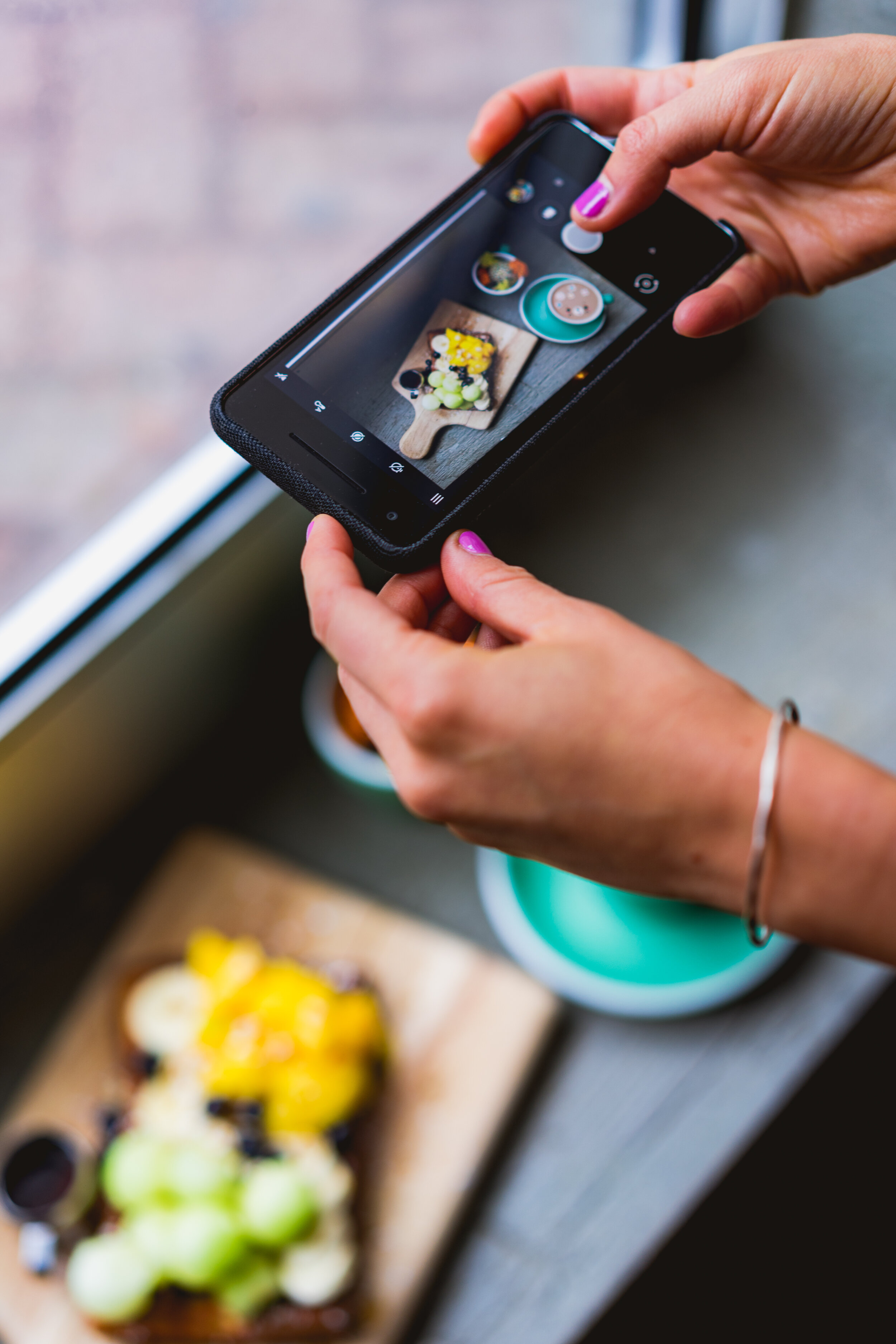 Women’s hands taking a photo of food on an iphone.