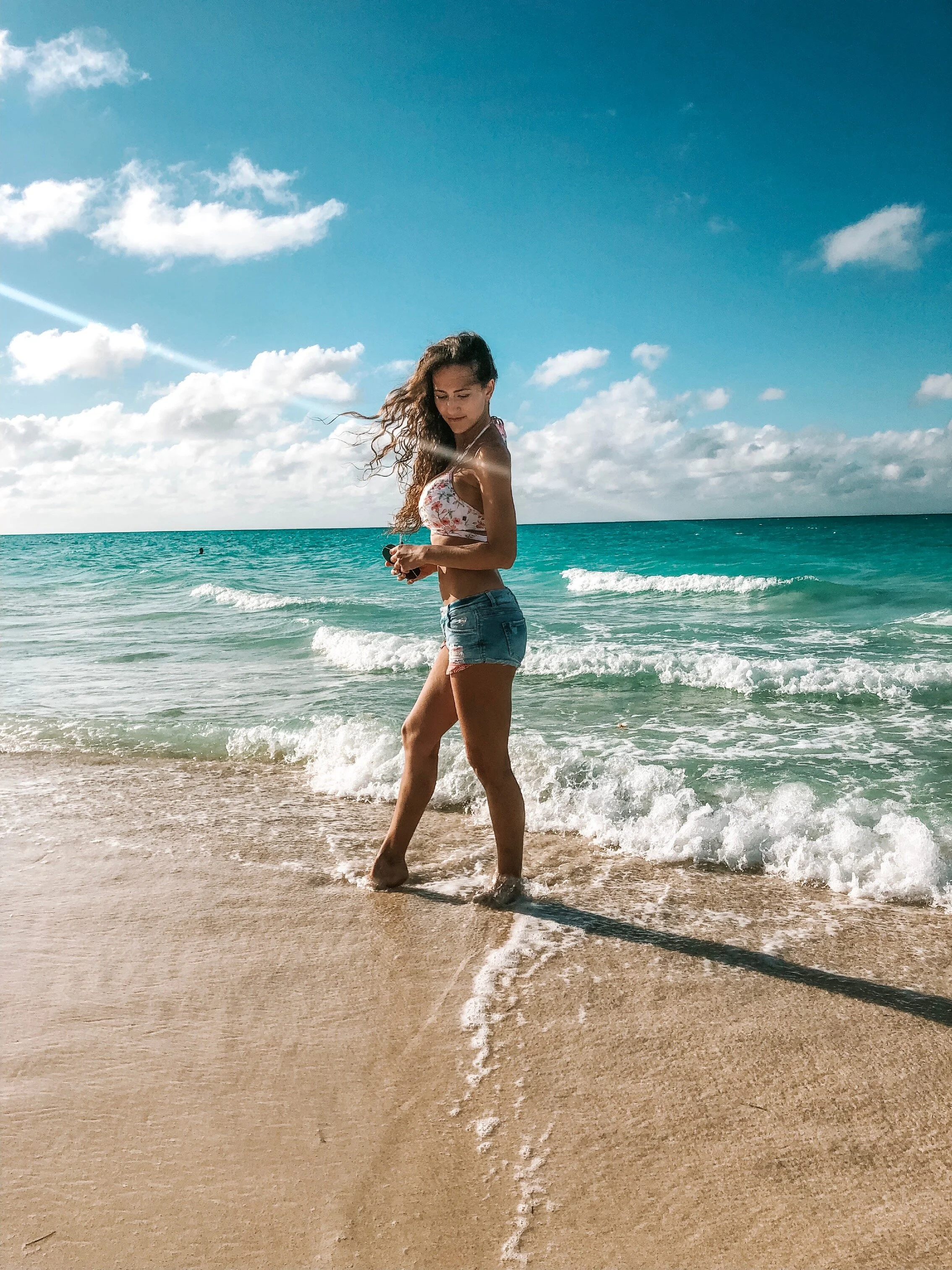 A woman with a bikini top and shorts standing on the beach during golden hour.