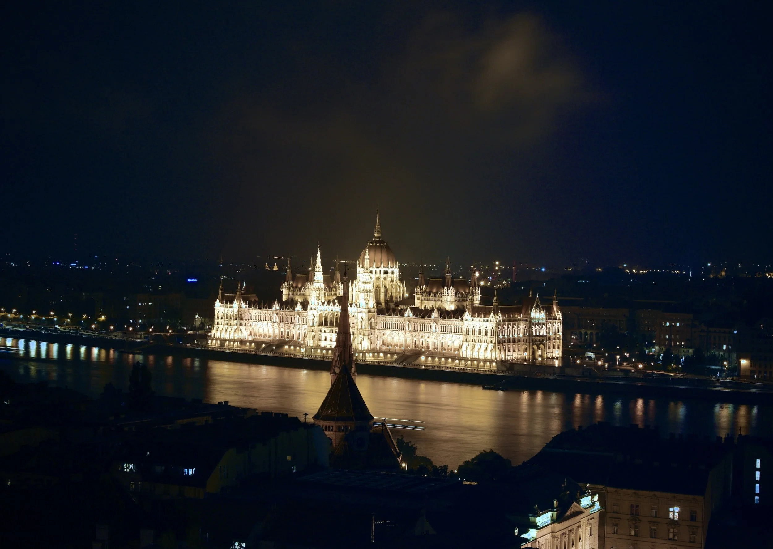 Night time city scape view of Budapest over the river lit up with evening lights.